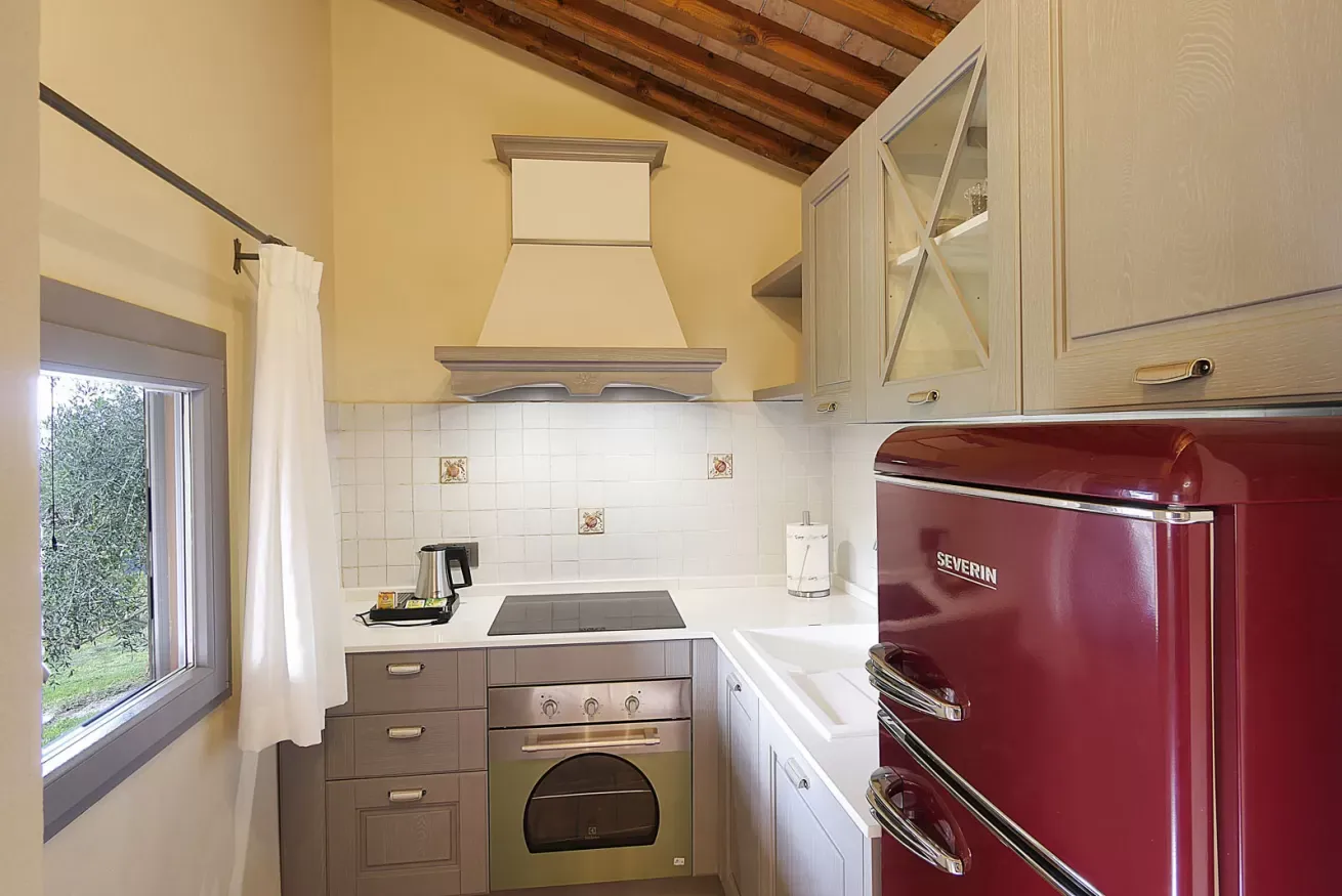 Cucina con mobili chiari, forno, piano cottura e frigorifero rosso retrò