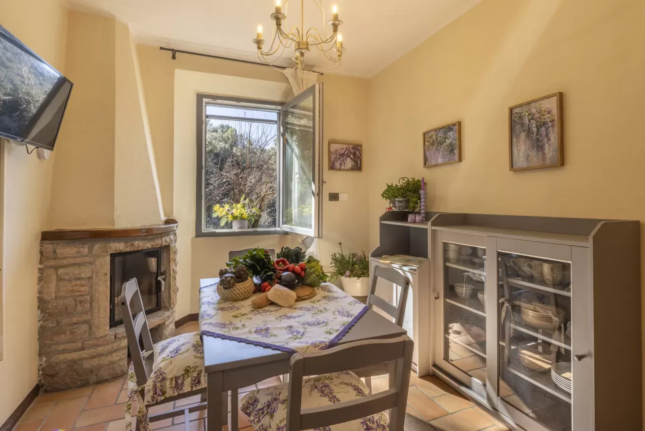 Sala da pranzo luminosa con tavolo apparecchiato, camino in pietra e finestra aperta sul giardino