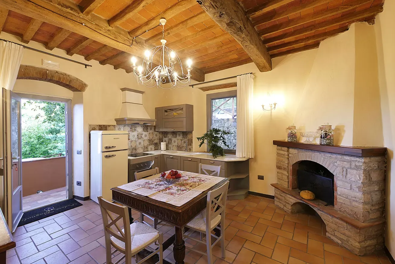Cucina rustica con tavolo da pranzo, camino in pietra, soffitto con travi a vista e porta aperta sul verde