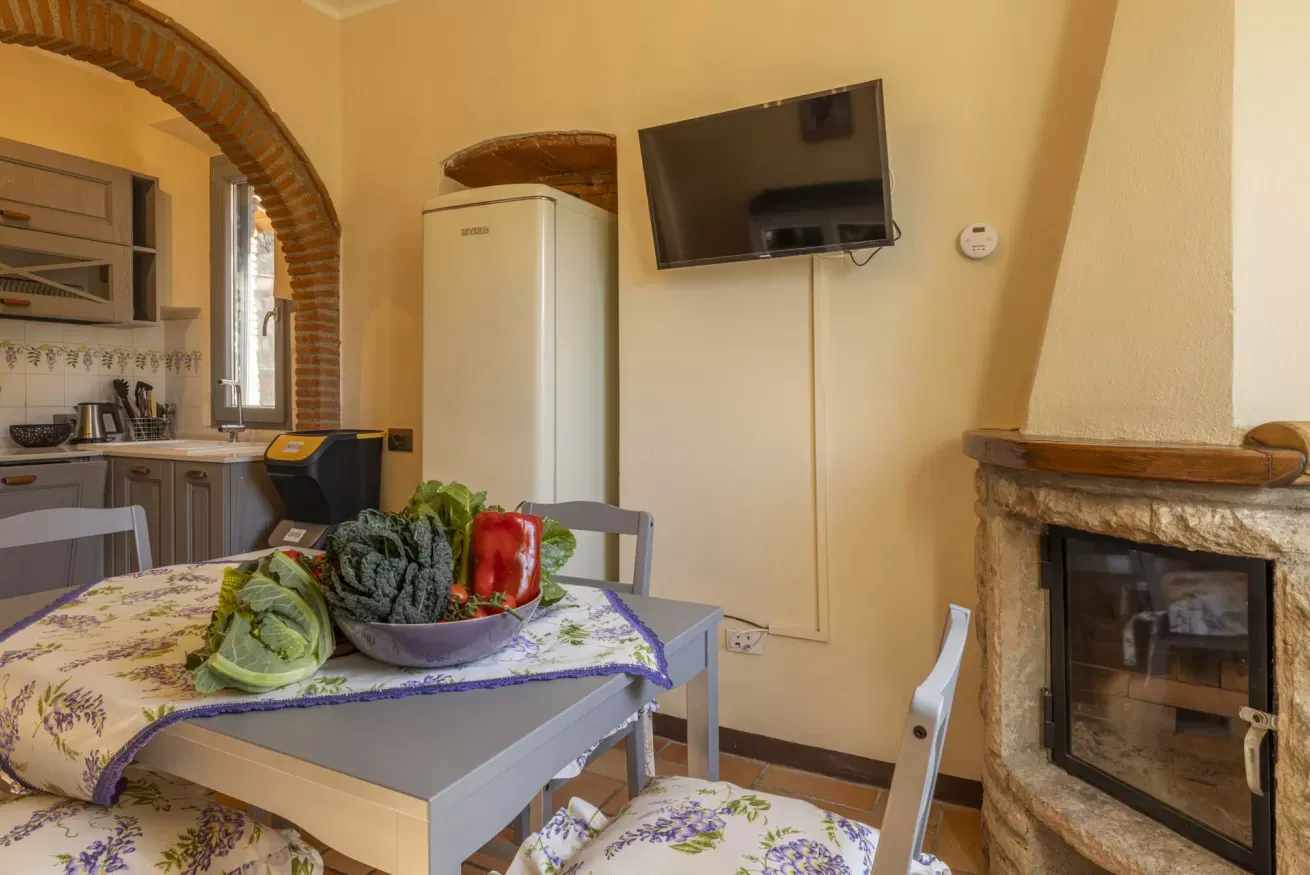 Cucina con tavolo apparecchiato, verdure fresche, frigorifero, TV a parete e camino in pietra