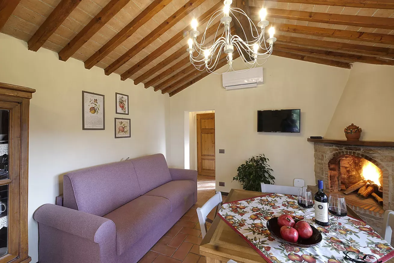 Soggiorno rustico con camino acceso, divano viola e tavolo apparecchiato
