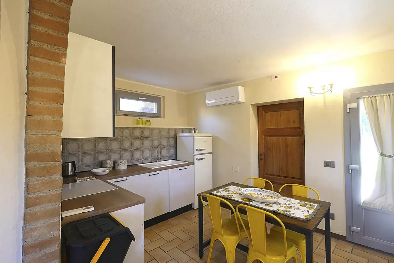 Cucina con tavolo da pranzo, sedie gialle, frigorifero e porta finestra