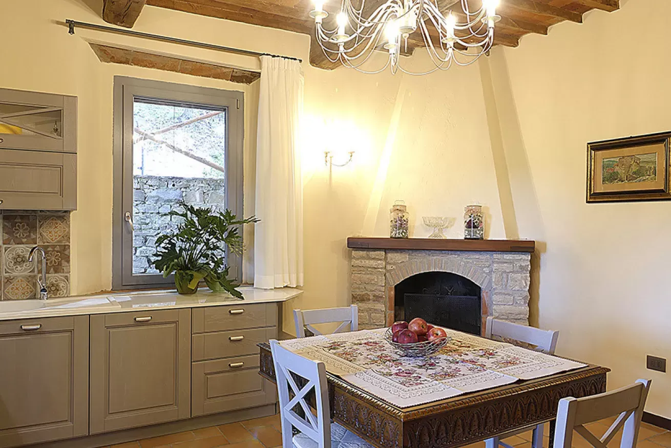 Cucina-soggiorno con tavolo da pranzo, camino in pietra, finestra e lampadario a bracci