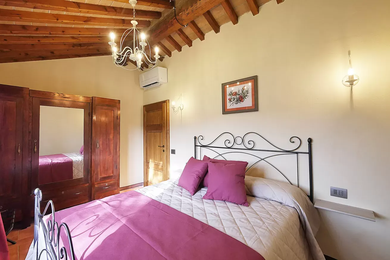 Camera da letto con letto matrimoniale, armadio in legno, soffitto con travi a vista e lampadario