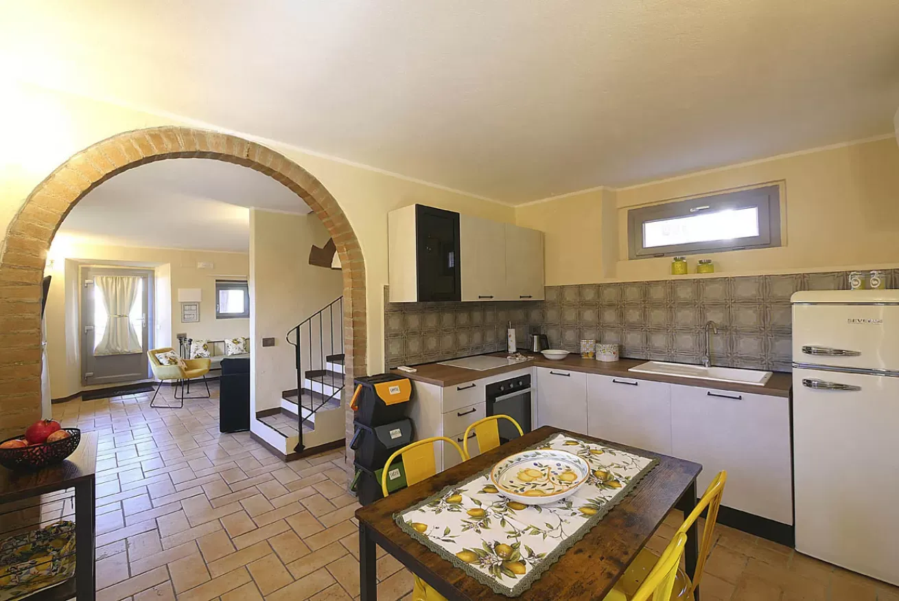 Cucina e zona pranzo in stile rustico con arco in mattoni e scala interna