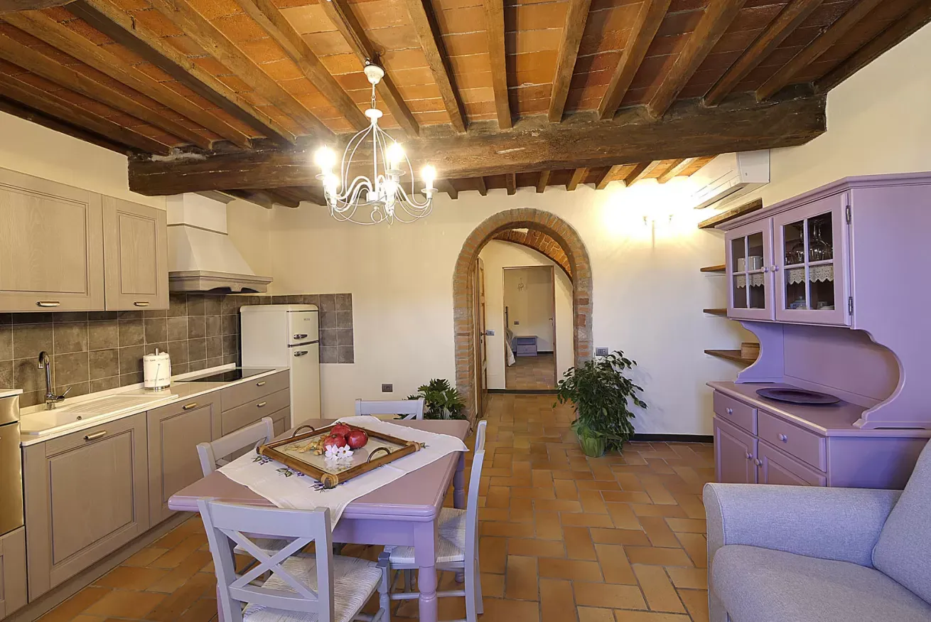 Cucina-soggiorno rustica con travi a vista, tavolo da pranzo e arredi lilla