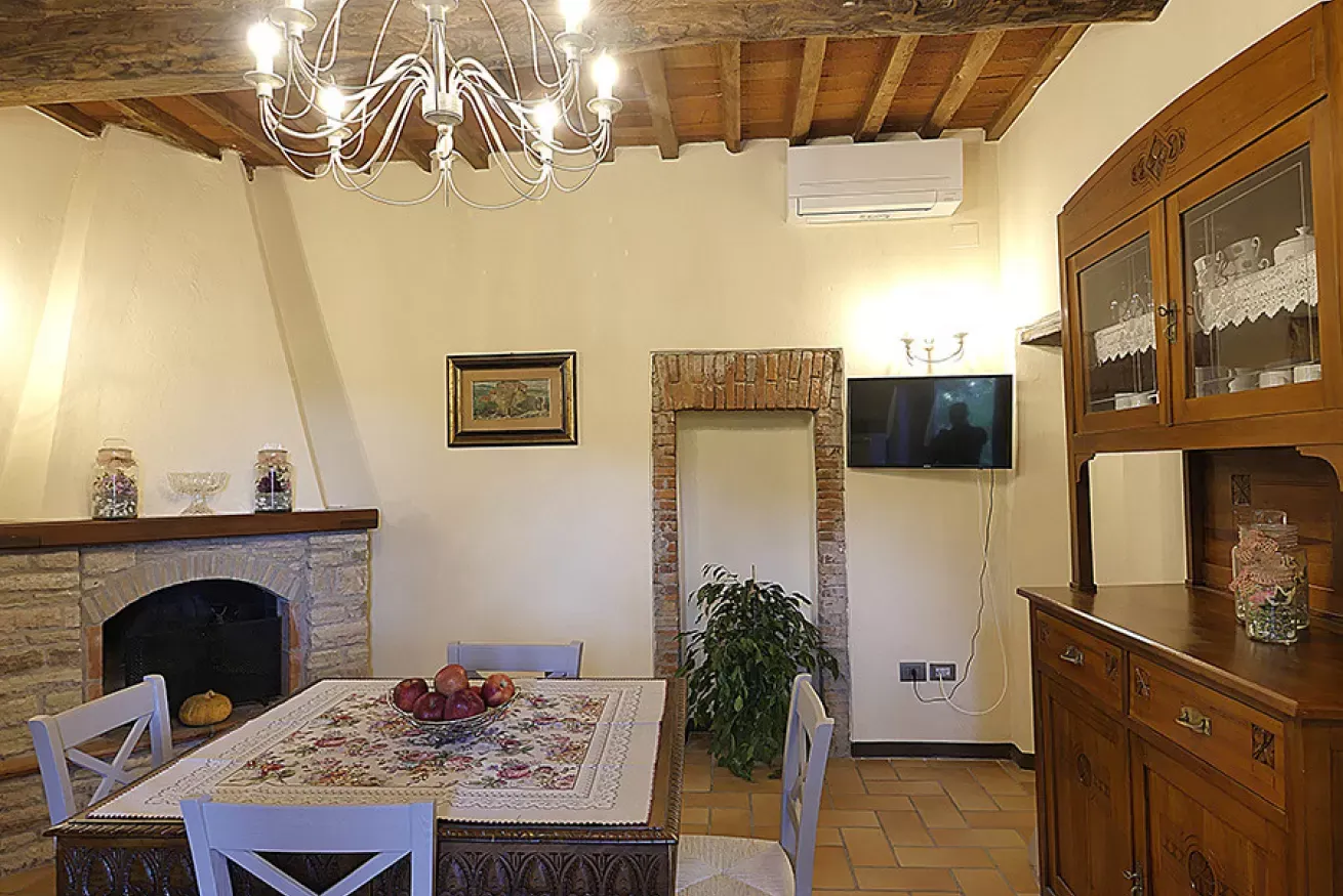 Sala da pranzo rustica con tavolo apparecchiato, camino, TV a parete e credenza in legno