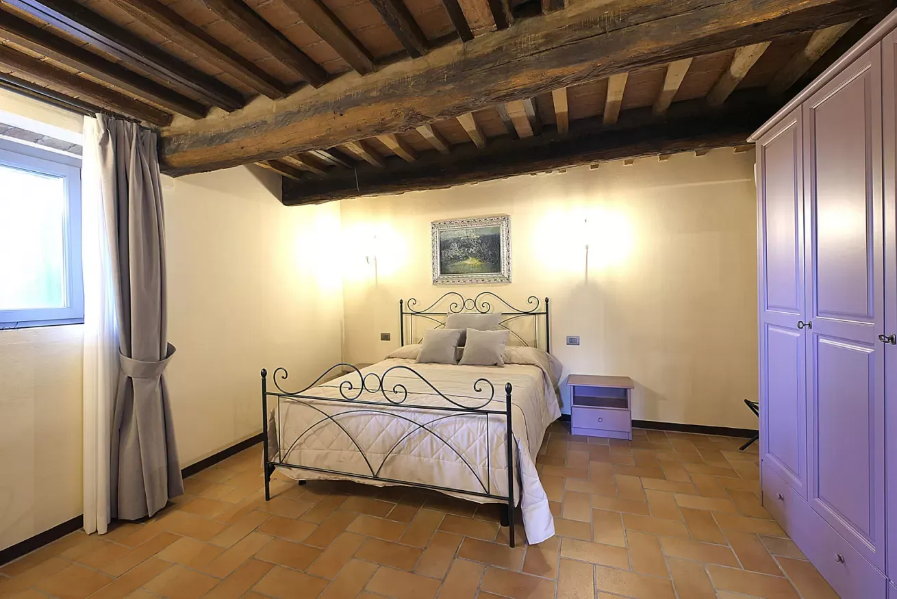 Camera da letto con letto matrimoniale, travi in legno a vista e armadio lilla