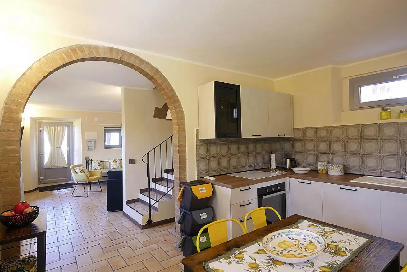 Interno di cucina e soggiorno con arco in mattoni, tavolo apparecchiato e scala
