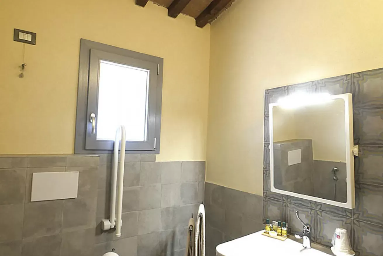 Bagno con finestra, specchio illuminato e lavandino con alcuni accessori