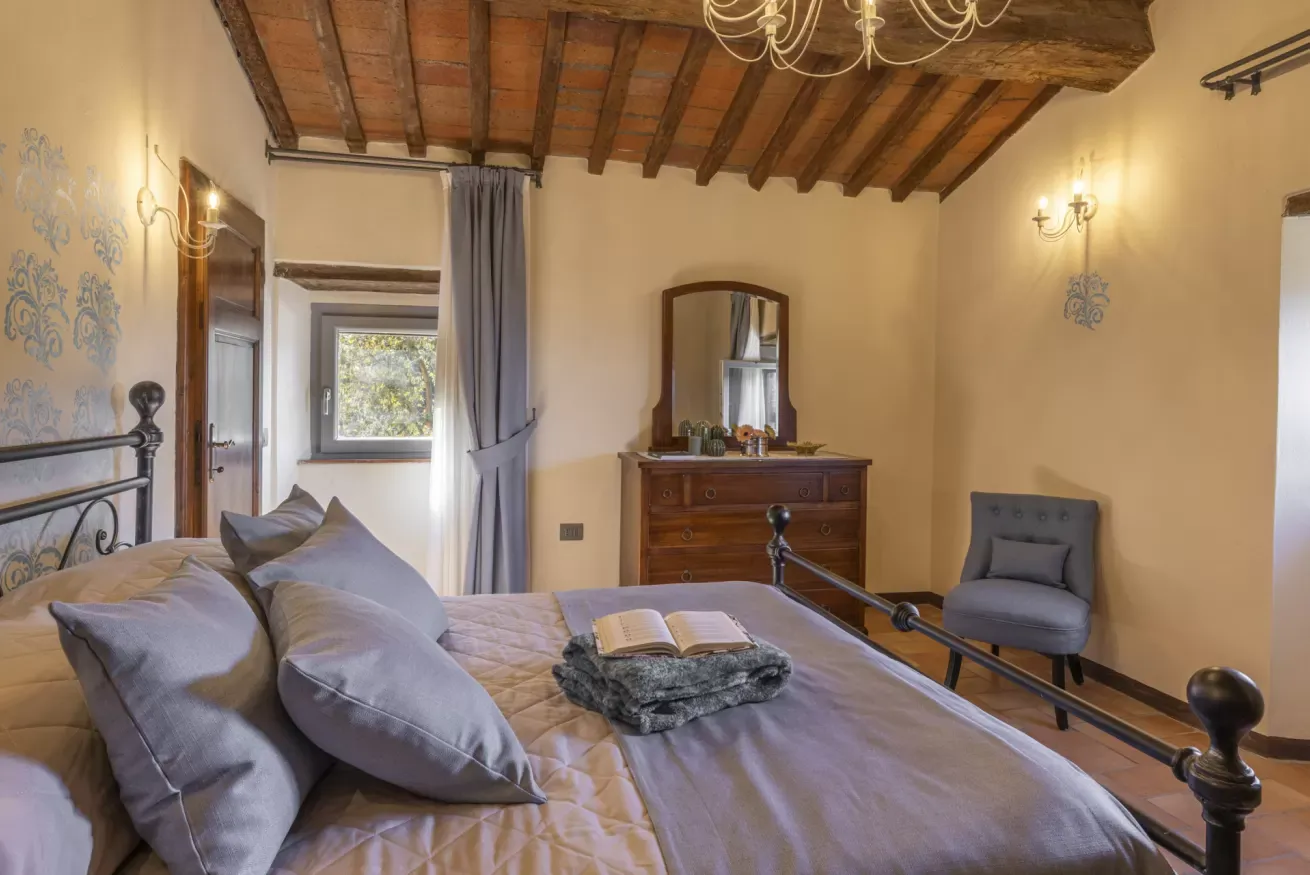 Camera da letto rustica con letto in ferro, travi a vista, cassettiera e poltrona