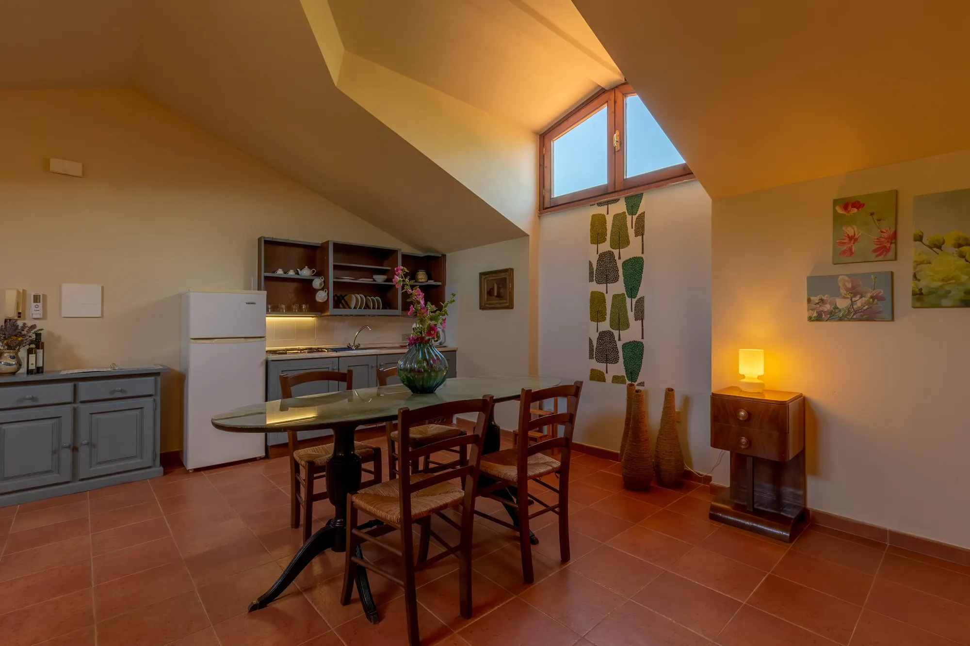Sala da pranzo e cucina mansardata con tavolo, sedie, frigorifero e finestra alta