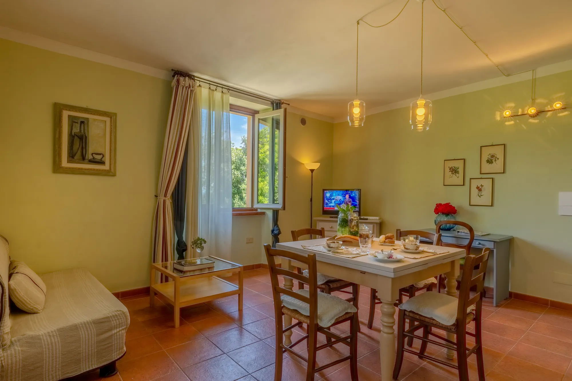 Soggiorno con tavolo da pranzo apparecchiato, finestra aperta e TV accesa in un ambiente luminoso
