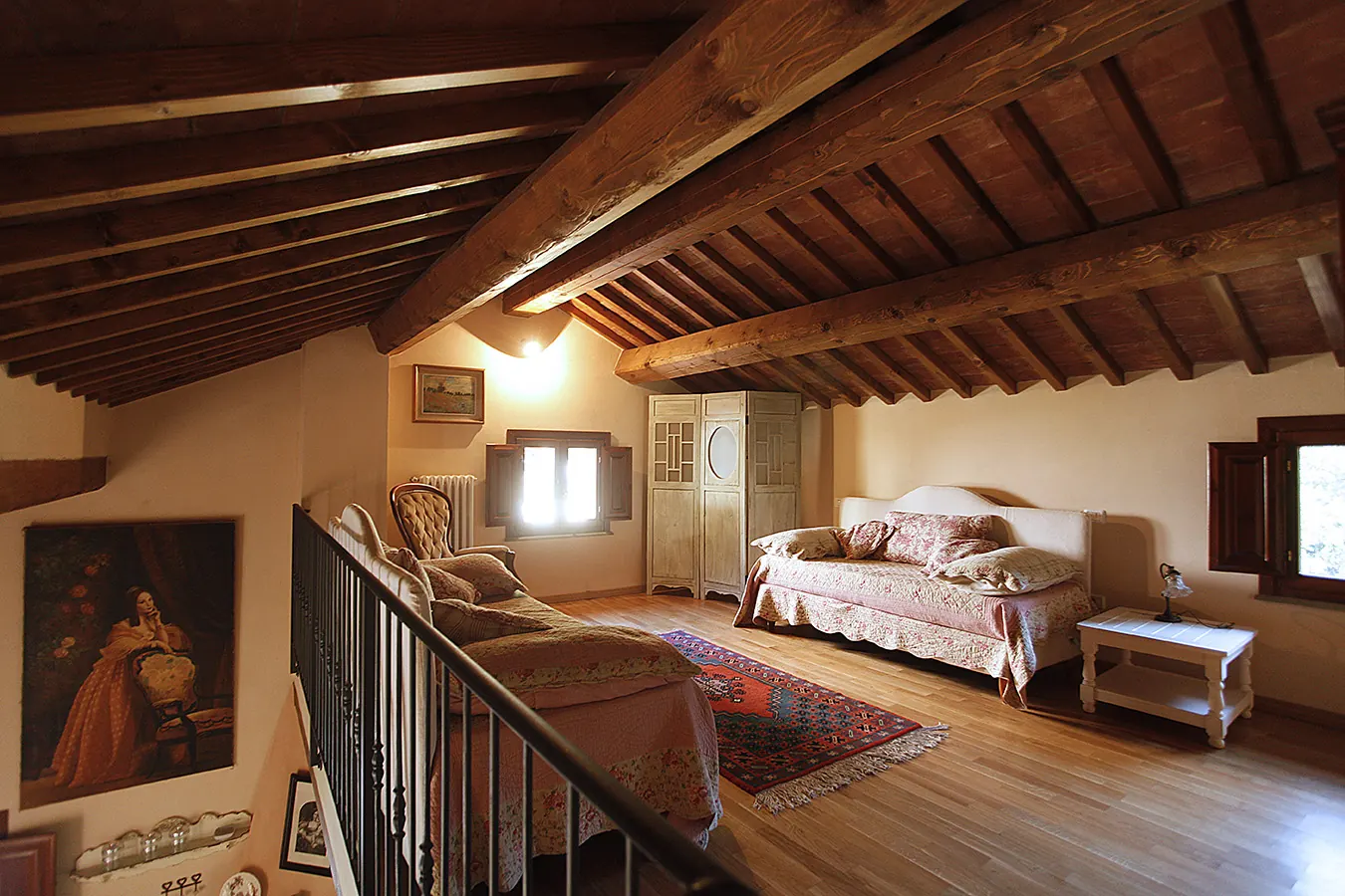 Camera mansardata arredata in stile rustico con travi in legno, letto, divano, armadio e finestra luminosa