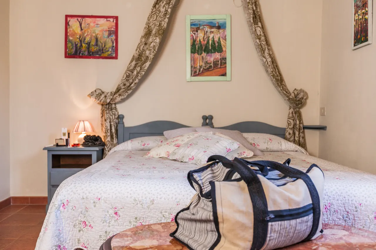 Camera da letto con letto matrimoniale, comodino con lampada e borsa da viaggio in primo piano