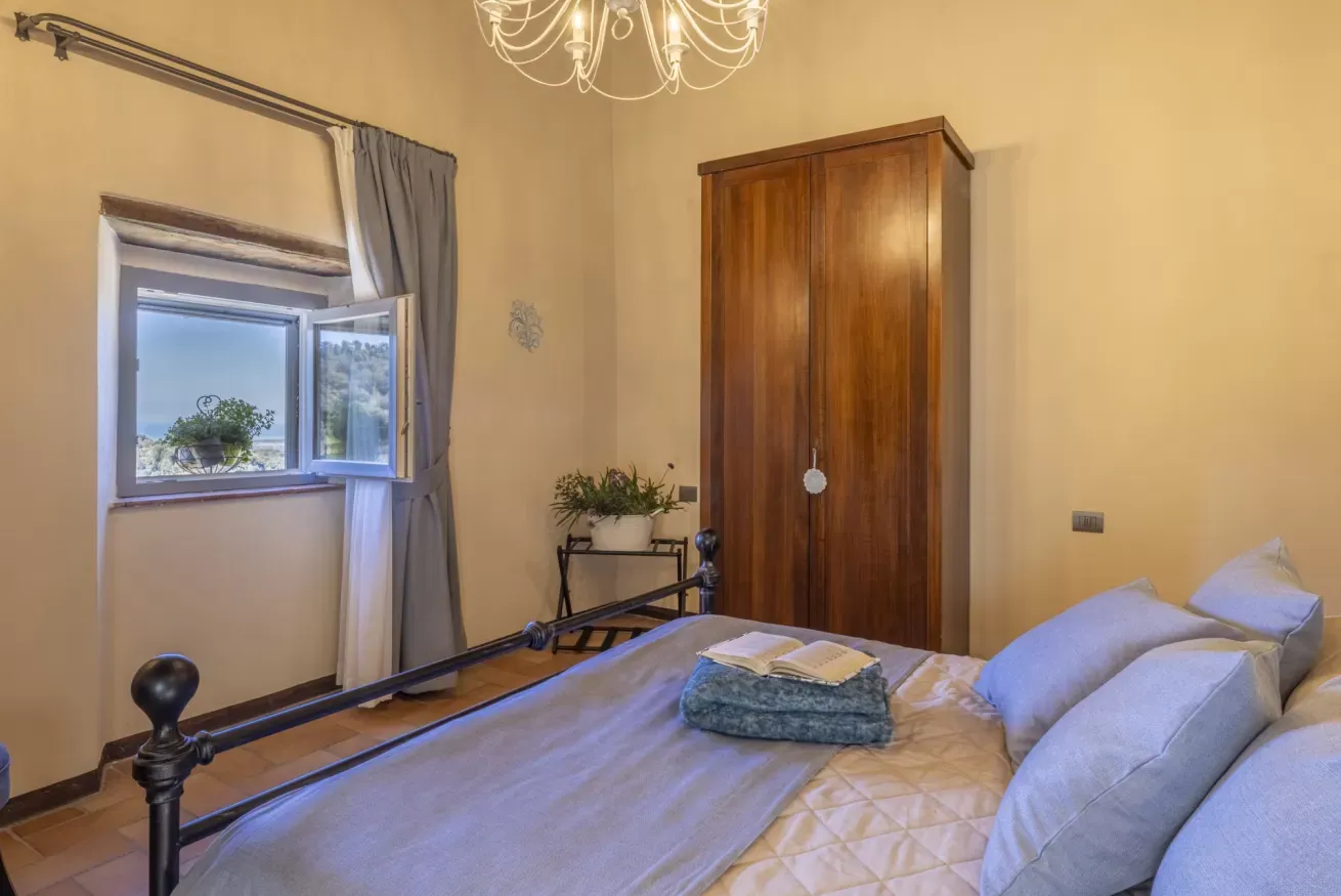 Camera da letto con letto matrimoniale, armadio in legno e finestra aperta con vista sul mare