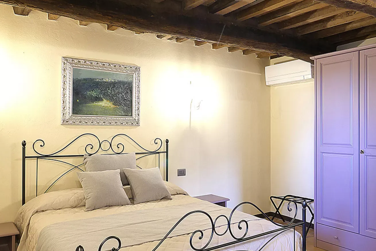 Camera da letto con letto in ferro battuto, armadio lilla e travi in legno a vista
