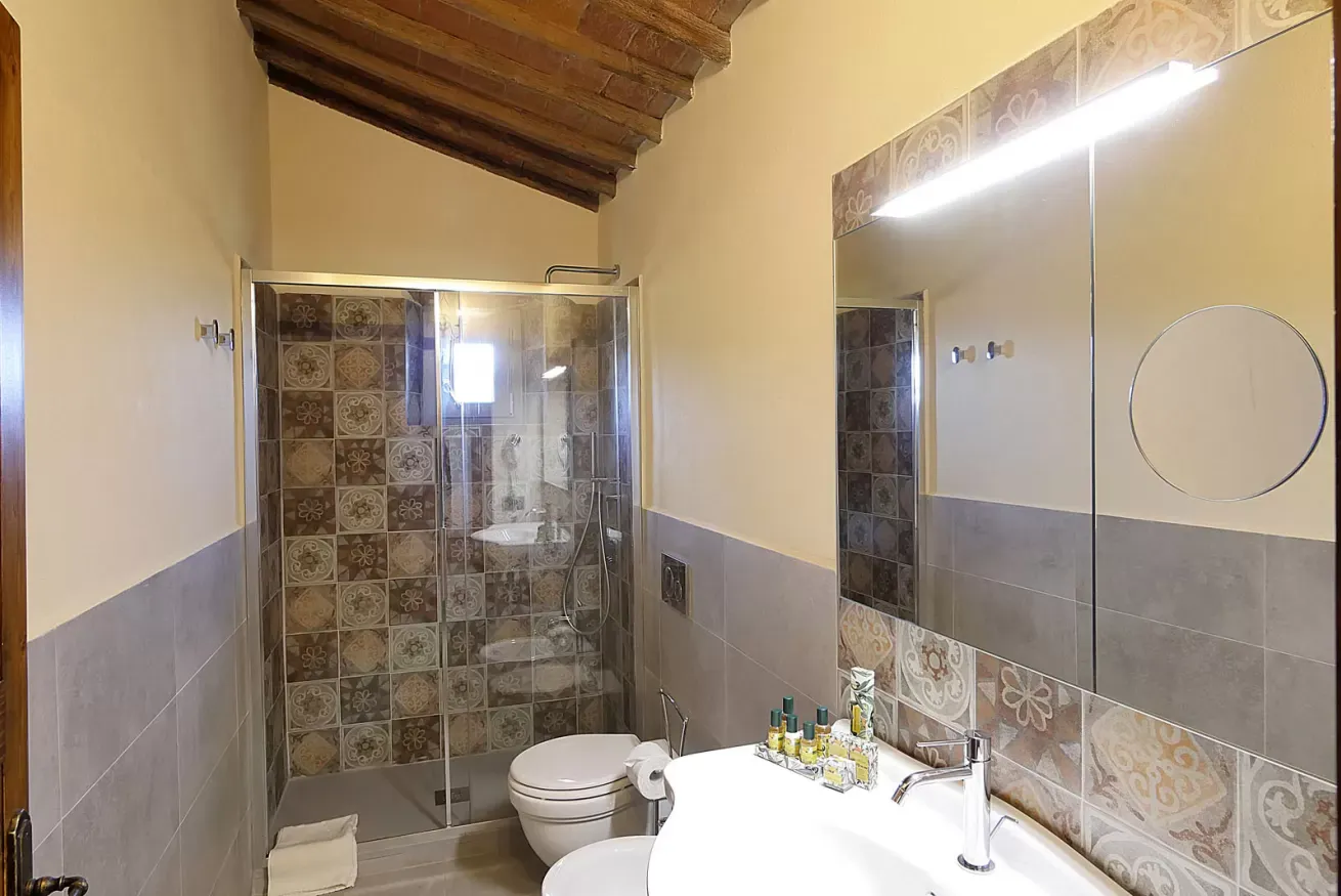Bagno con doccia in vetro, lavabo, specchio e soffitto con travi in legno