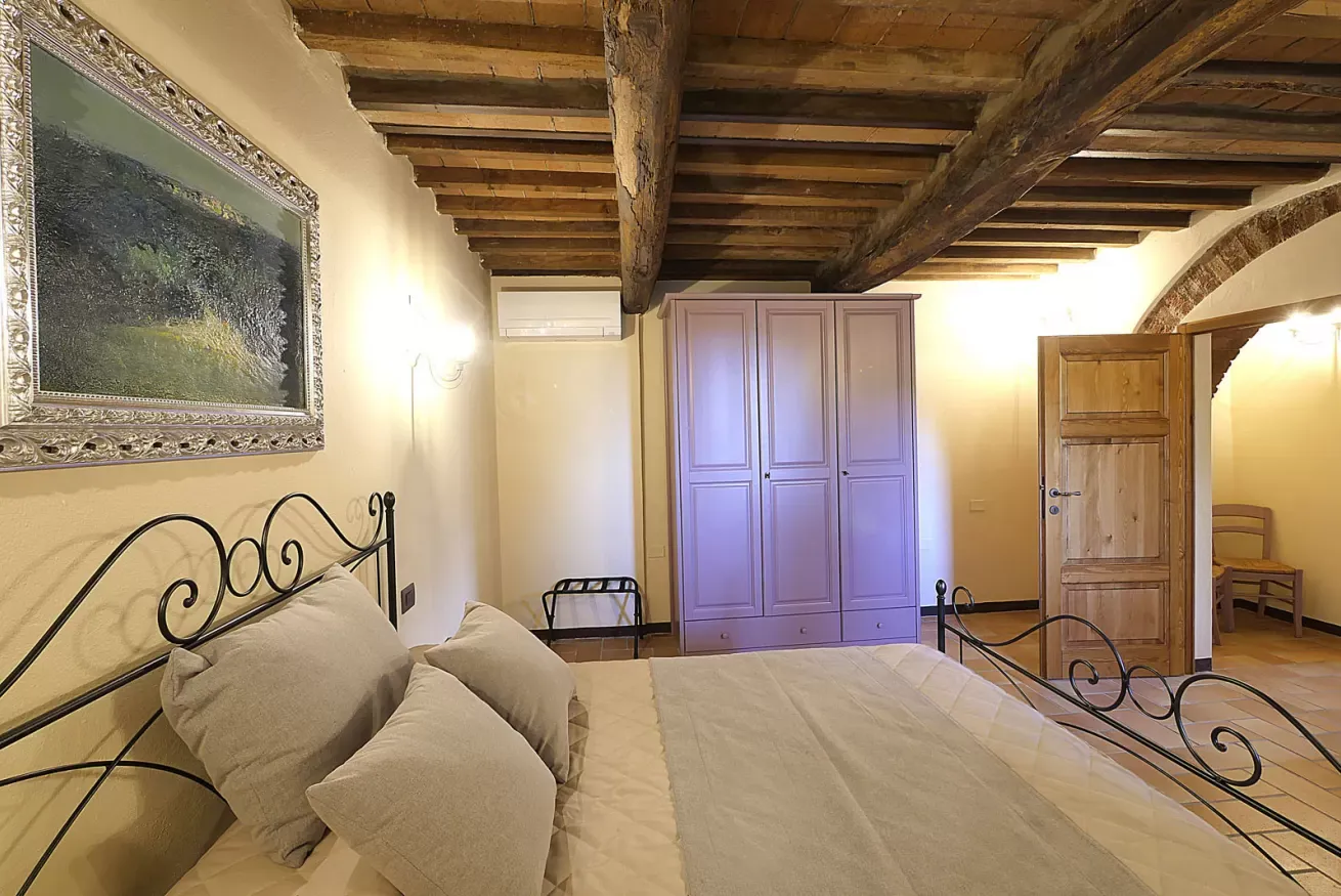 Camera da letto rustica con letto in ferro battuto, armadio lilla e soffitto con travi in legno a vista