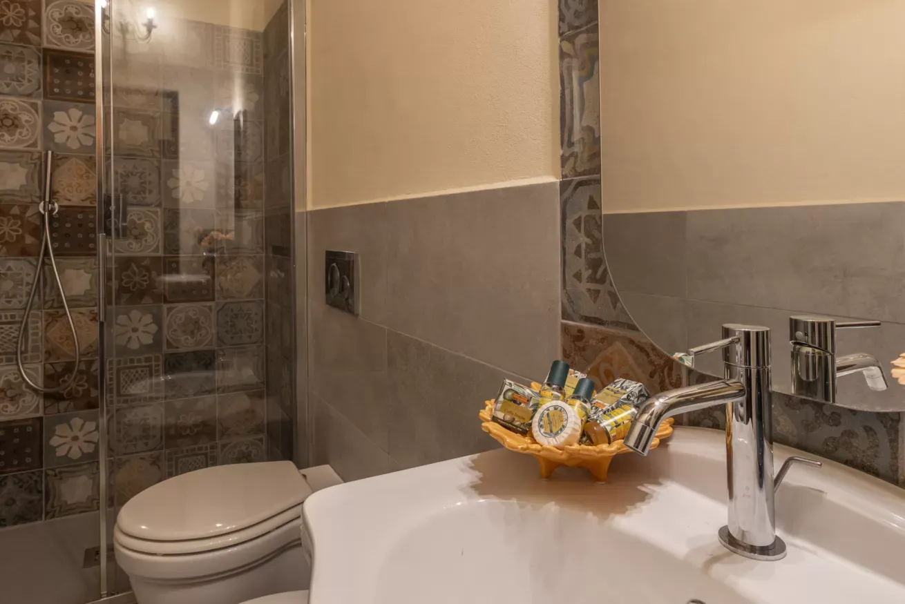 Bagno con doccia in vetro, lavabo con specchio e set di cortesia sul piano