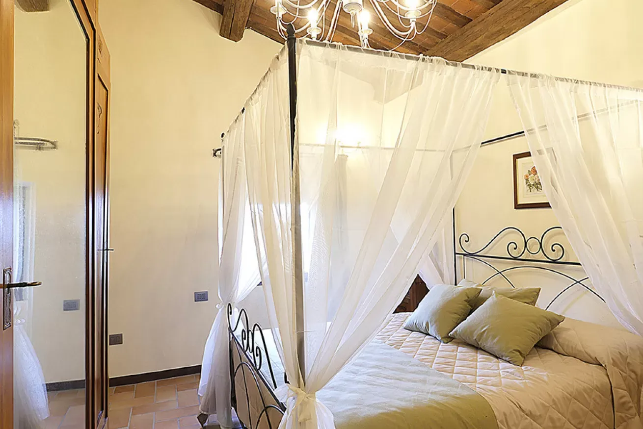 Camera da letto con letto a baldacchino, zanzariera bianca e cuscini verdi in una stanza rustica e luminosa