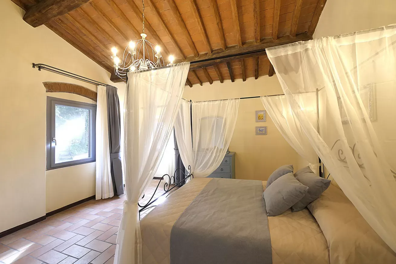 Camera da letto con letto a baldacchino, soffitto in legno e finestra con tende chiare