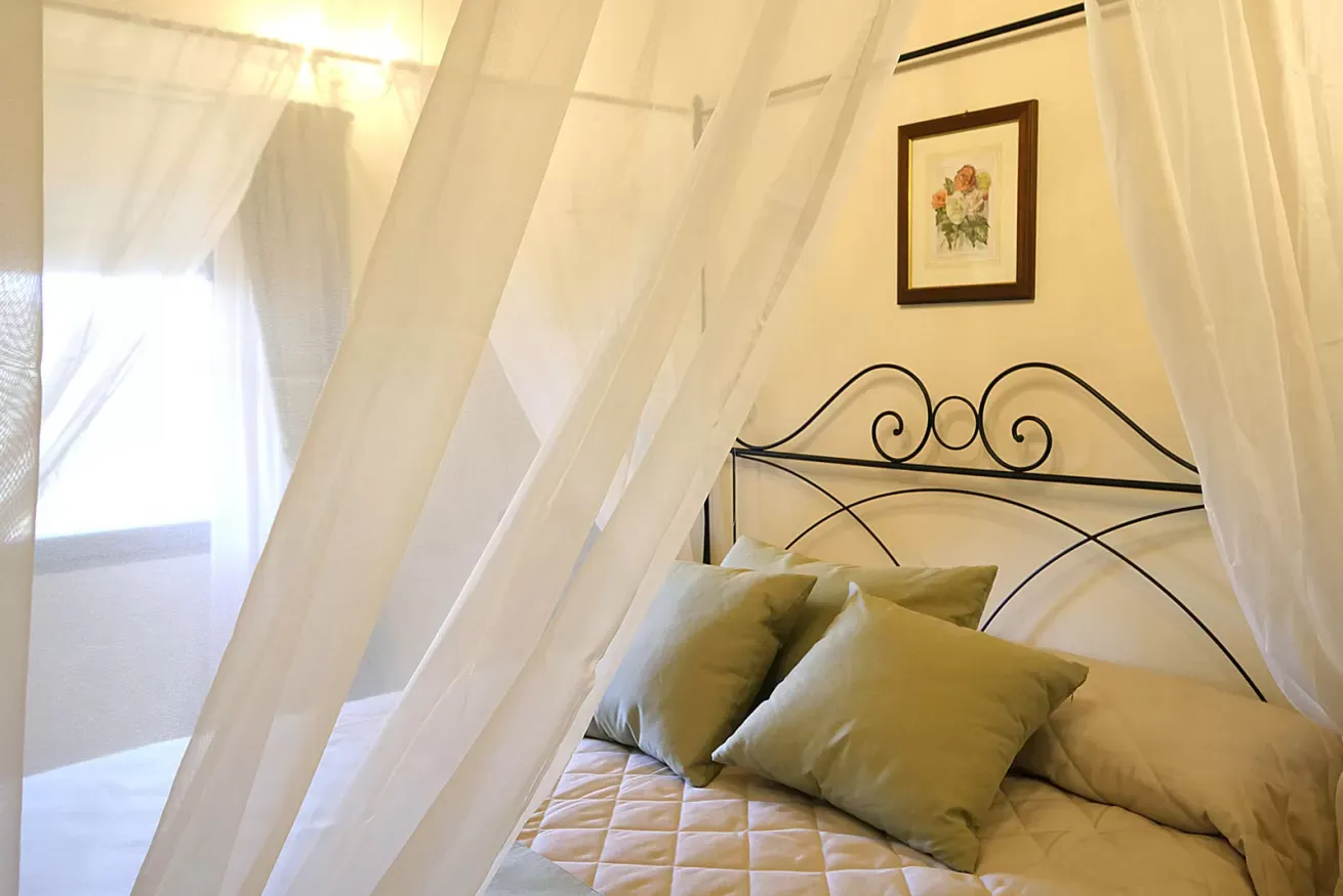 Camera da letto luminosa con letto a baldacchino, zanzariera bianca e cuscini verdi