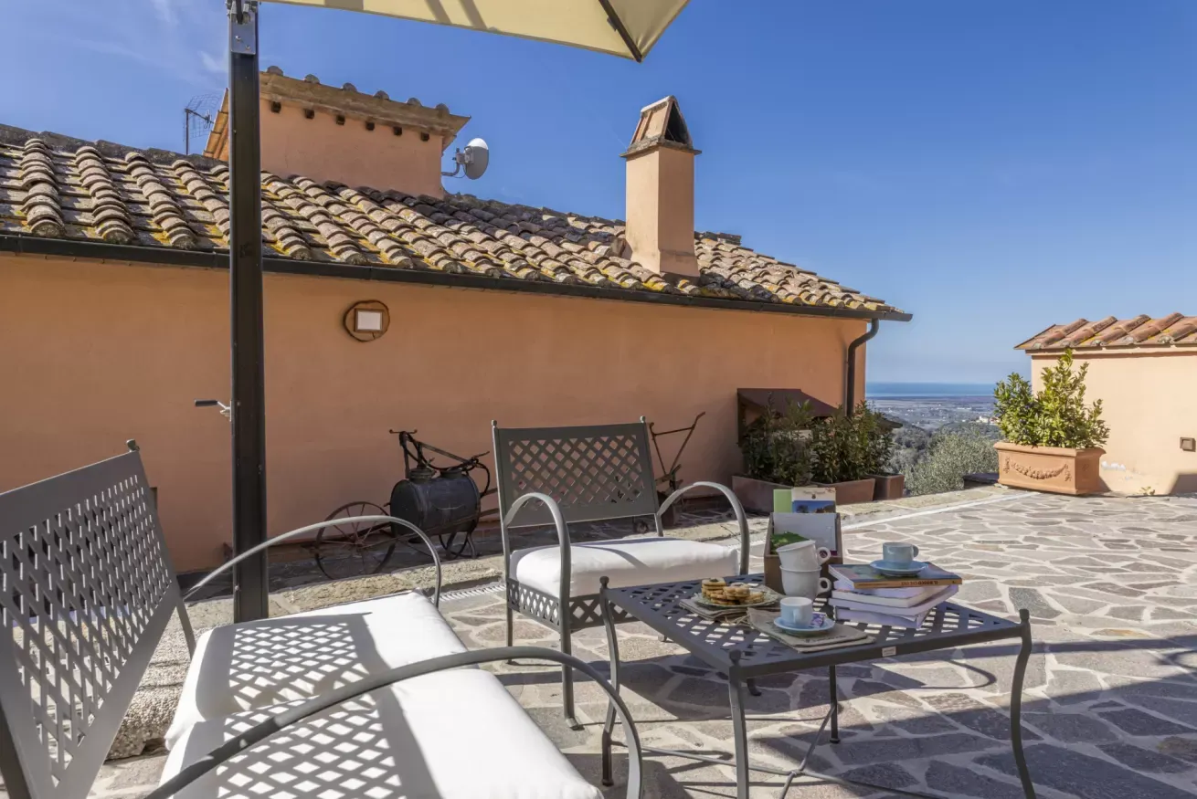 Terrazza all’aperto con tavolo apparecchiato, sedie e vista panoramica sul mare sotto un cielo sereno