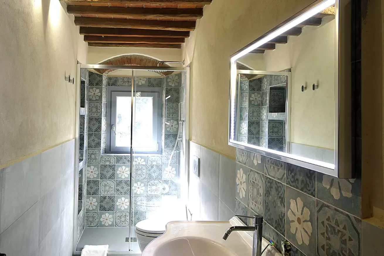 Bagno stretto con doccia in vetro, lavabo, specchio illuminato e finestra in fondo