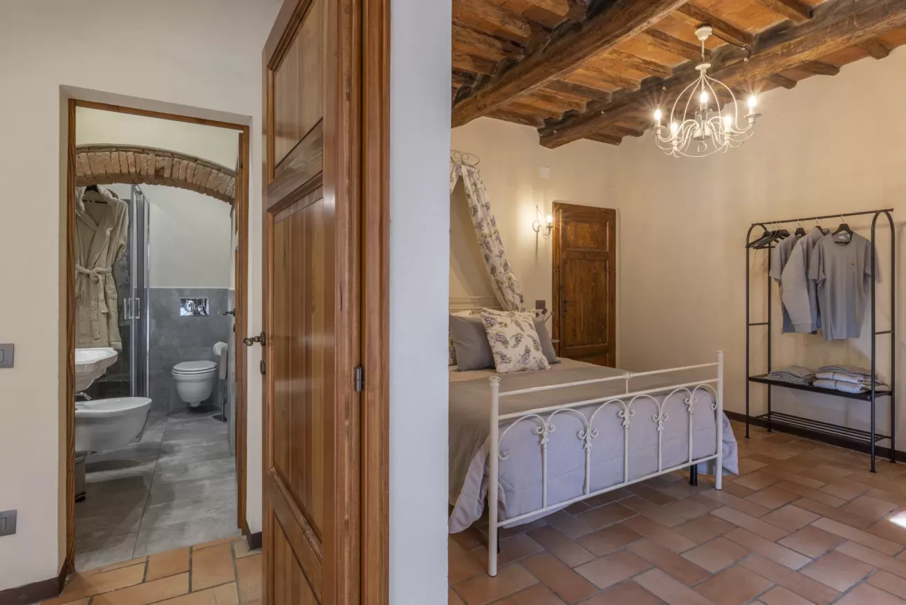 Camera da letto rustica con letto in ferro battuto, travi a vista e bagno en suite visibile dalla porta aperta