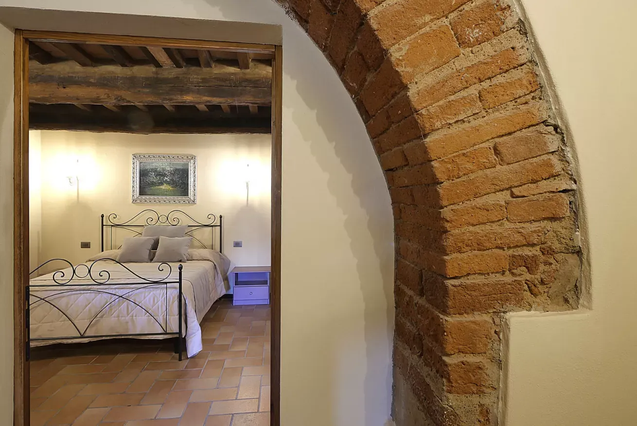 Camera da letto vista attraverso un arco in mattoni, con letto matrimoniale in ferro battuto