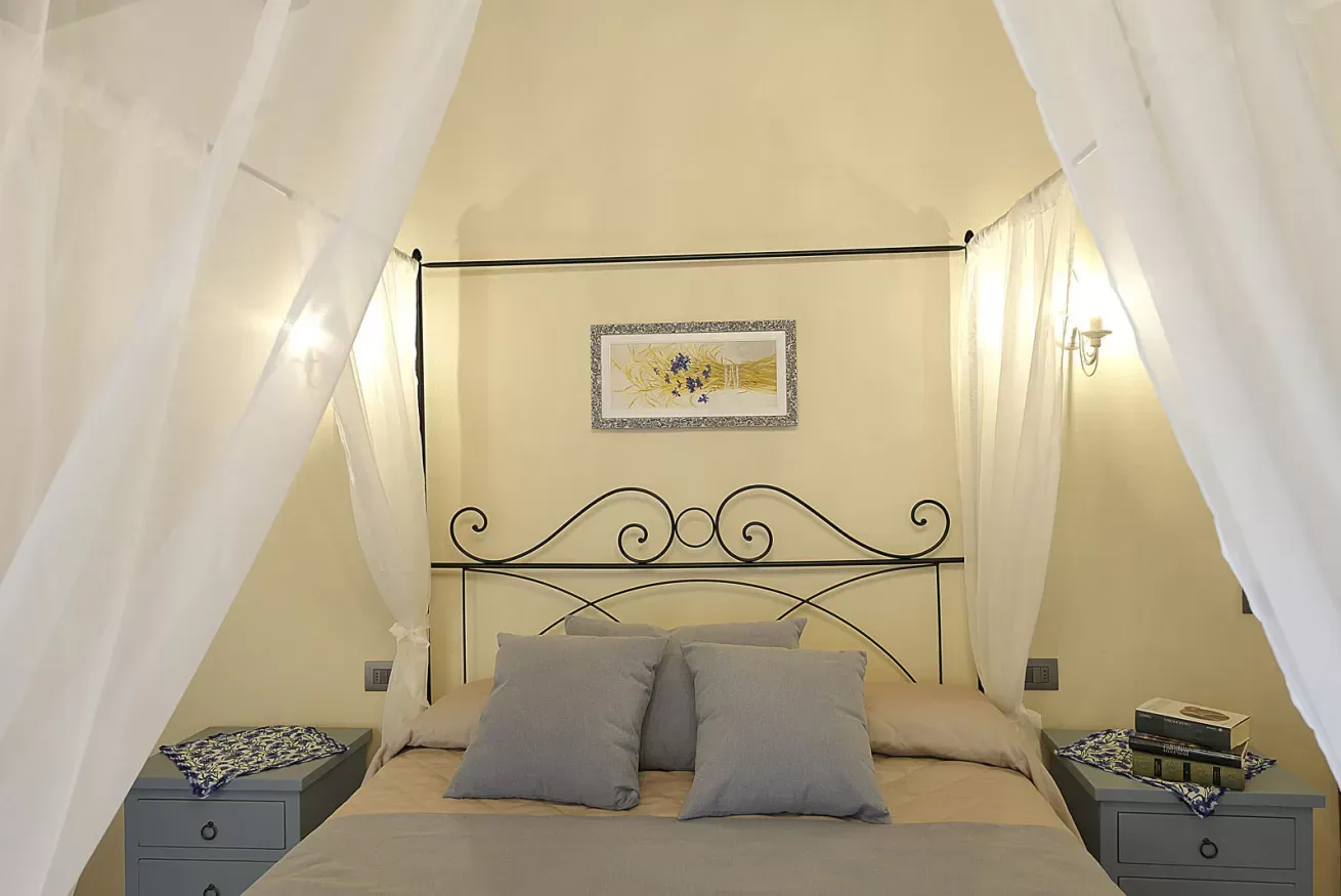 Camera da letto con letto a baldacchino, tende bianche e due comodini grigi