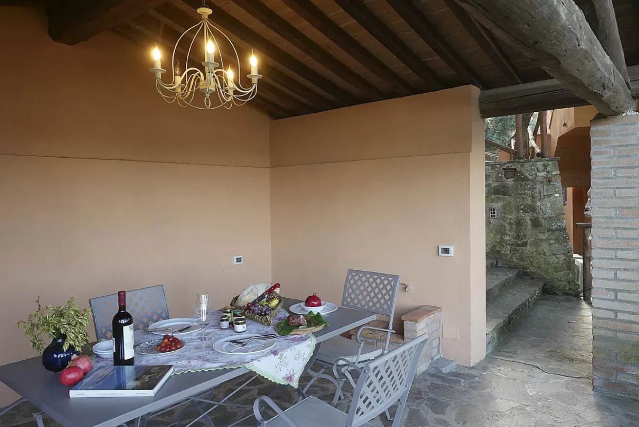 Tavolo apparecchiato sotto un portico con lampadario, sedie e vista su un passaggio in pietra