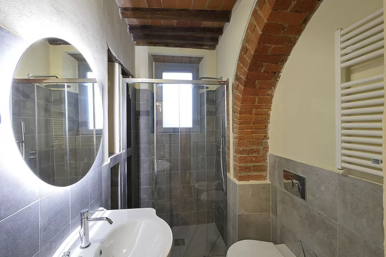 Bagno moderno con doccia in vetro, lavabo, specchio ovale e arco in mattoni a vista