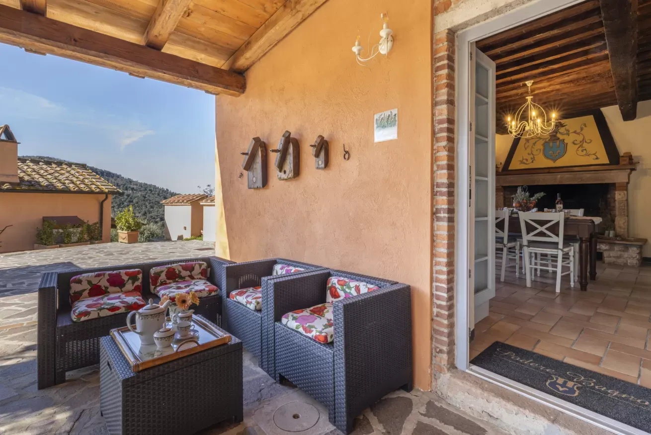 Terrazza coperta con salotto da esterno e vista sull’interno rustico della casa