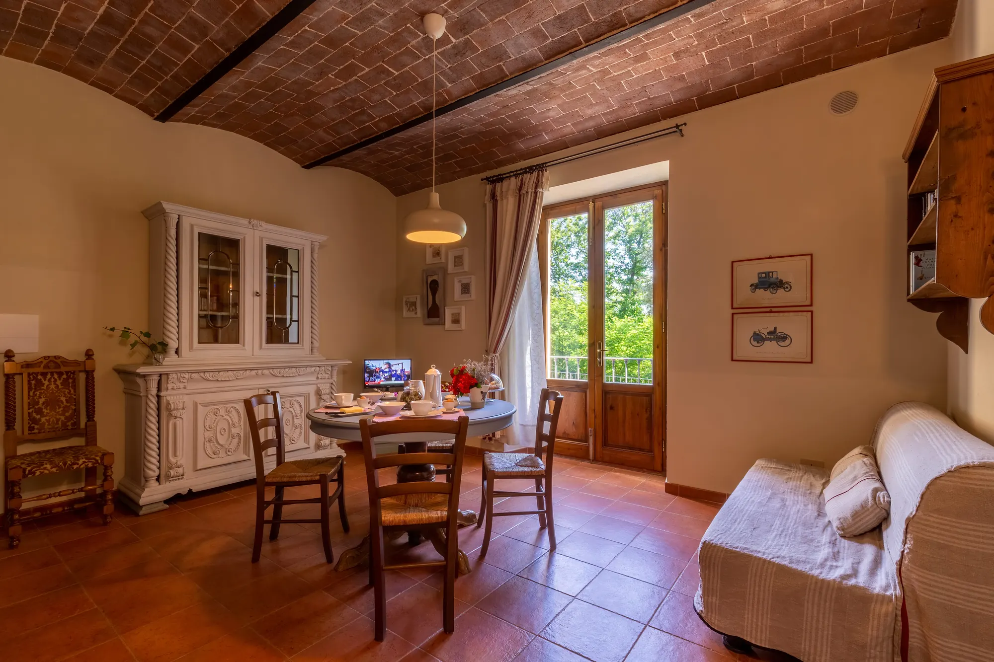 Soggiorno con tavolo apparecchiato, credenza bianca, divano e porta finestra aperta sul verde