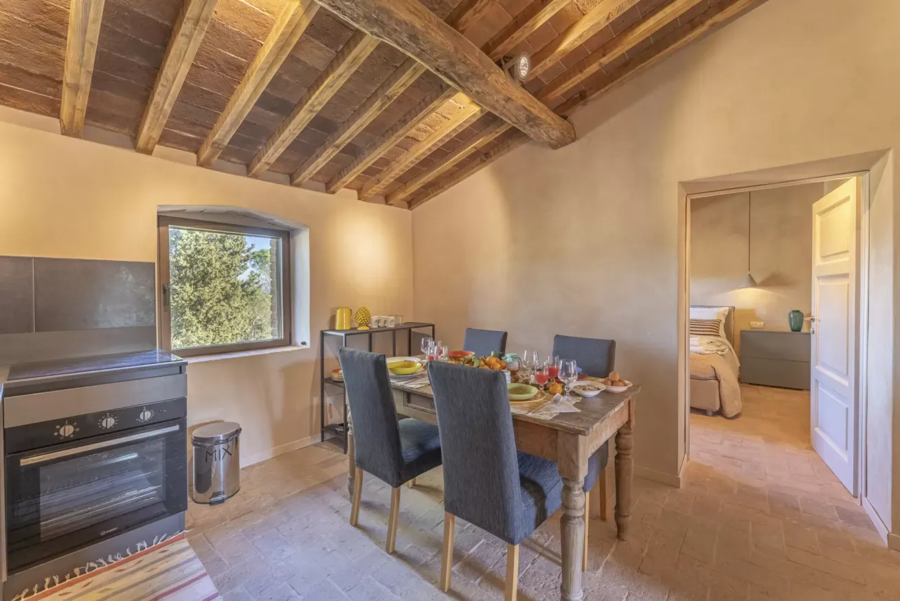 Cucina rustica con tavolo apparecchiato e camera da letto visibile attraverso la porta aperta