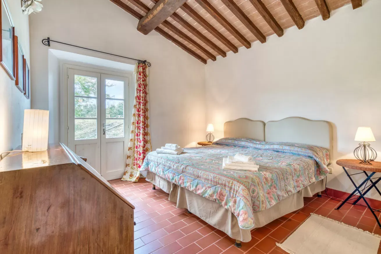Bedroom with a double bed, terracotta tile floor, exposed wood beams, and French doors to outside