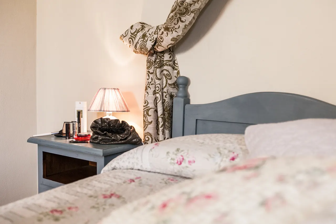 Camera da letto con comodino, lampada accesa e letto con biancheria floreale