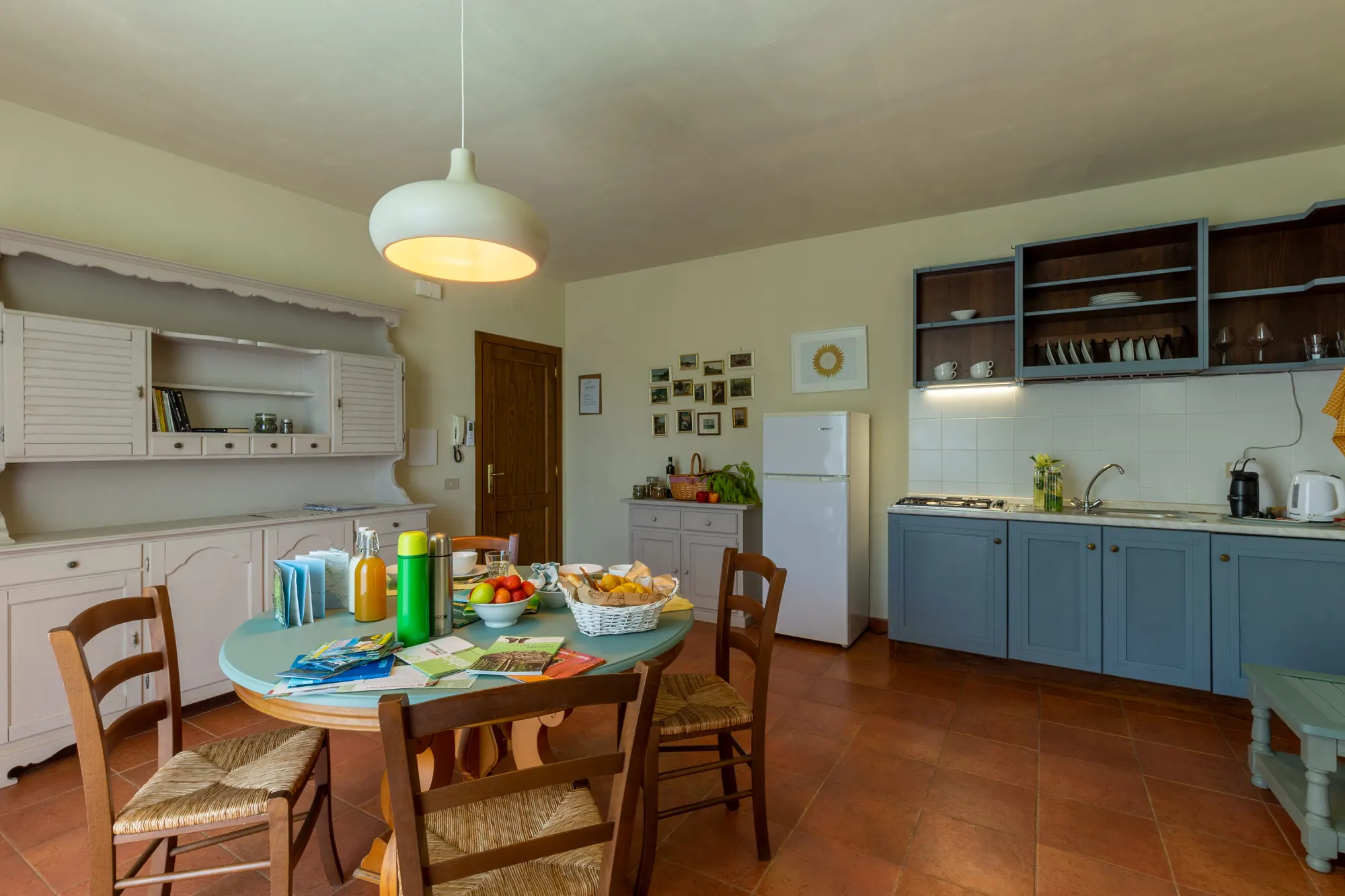 Cucina e zona pranzo con tavolo apparecchiato, mobili azzurri e bianchi e frigorifero bianco
