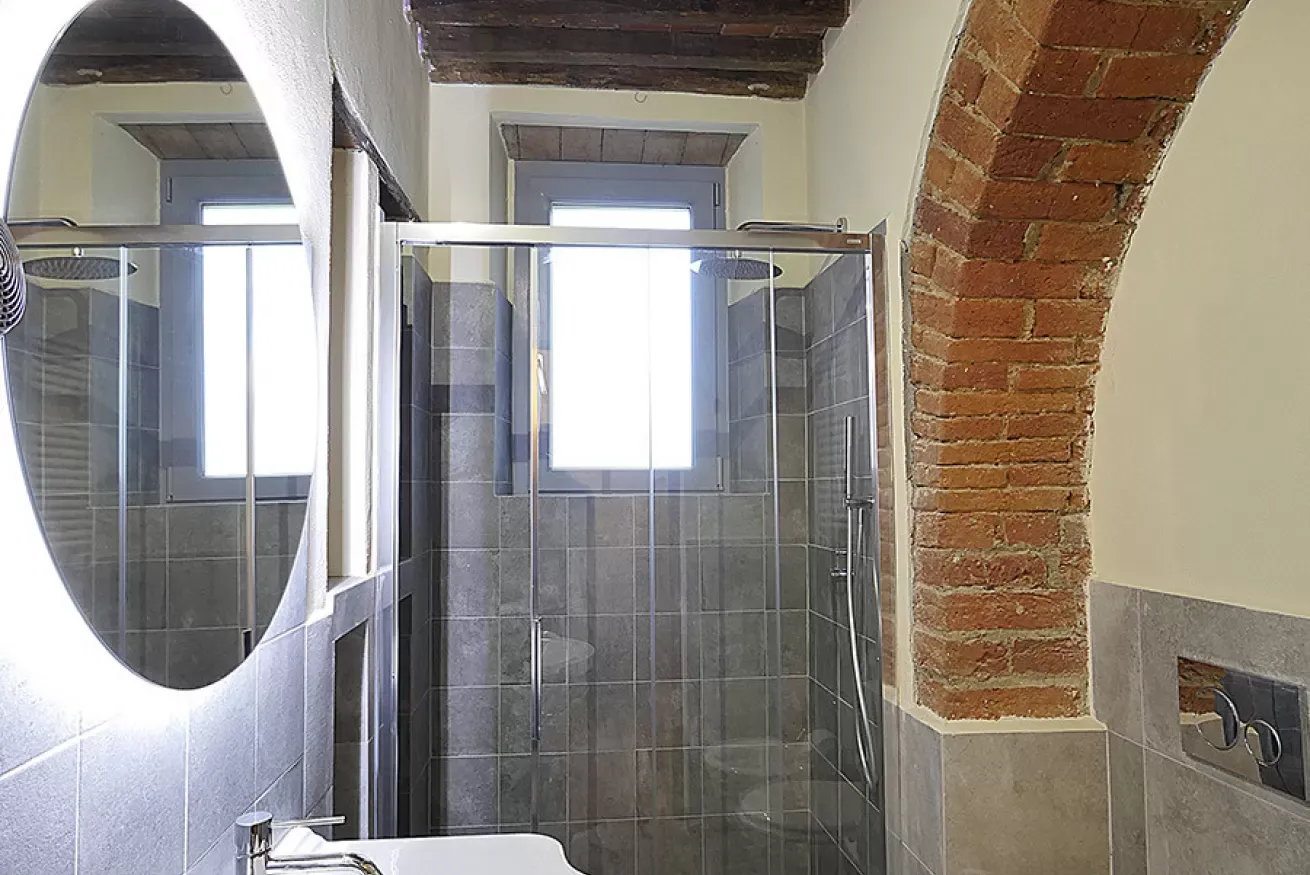 Bagno con doccia in vetro, specchio ovale e arco in mattoni a vista