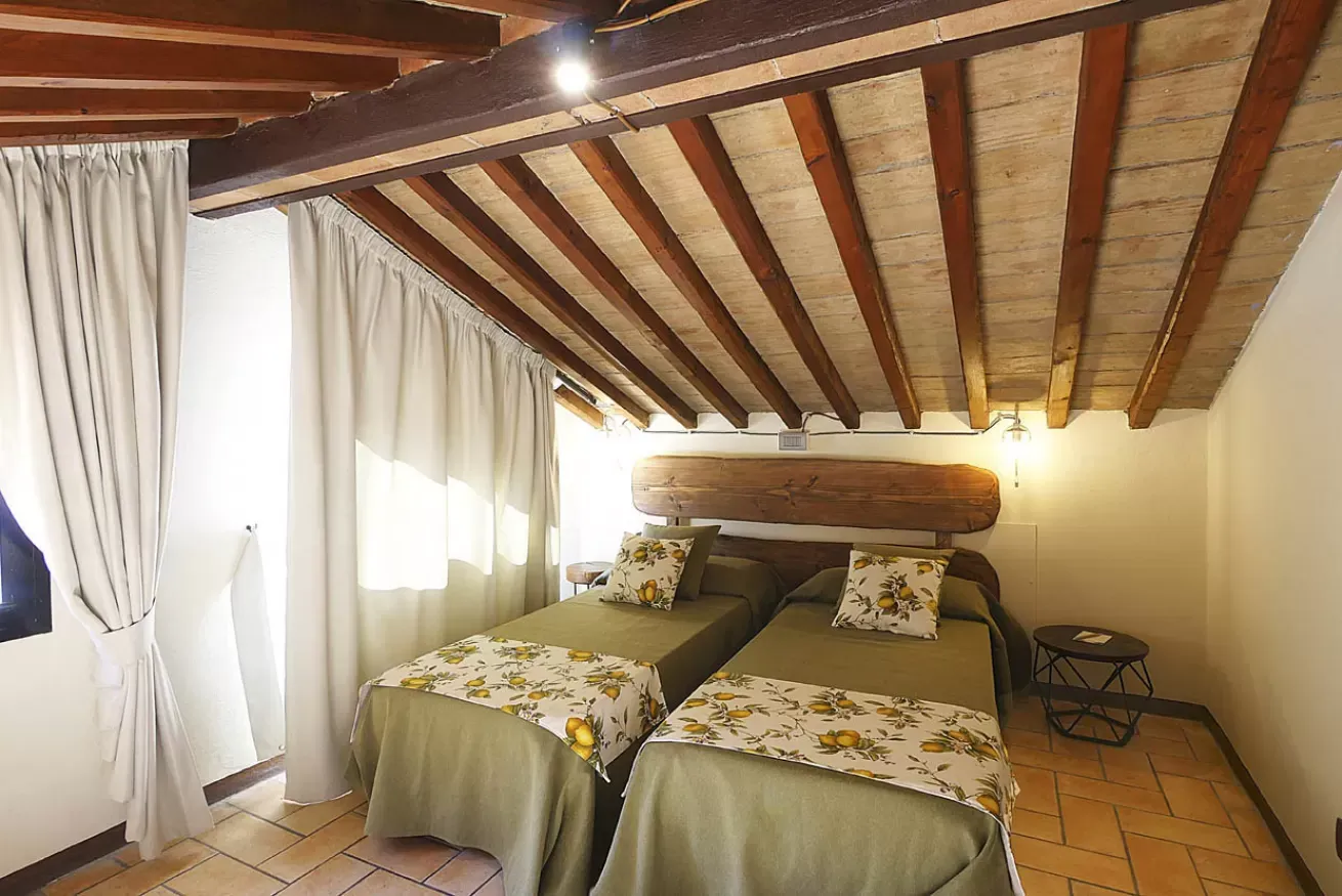 Camera da letto con due letti singoli, soffitto con travi in legno e tende chiare