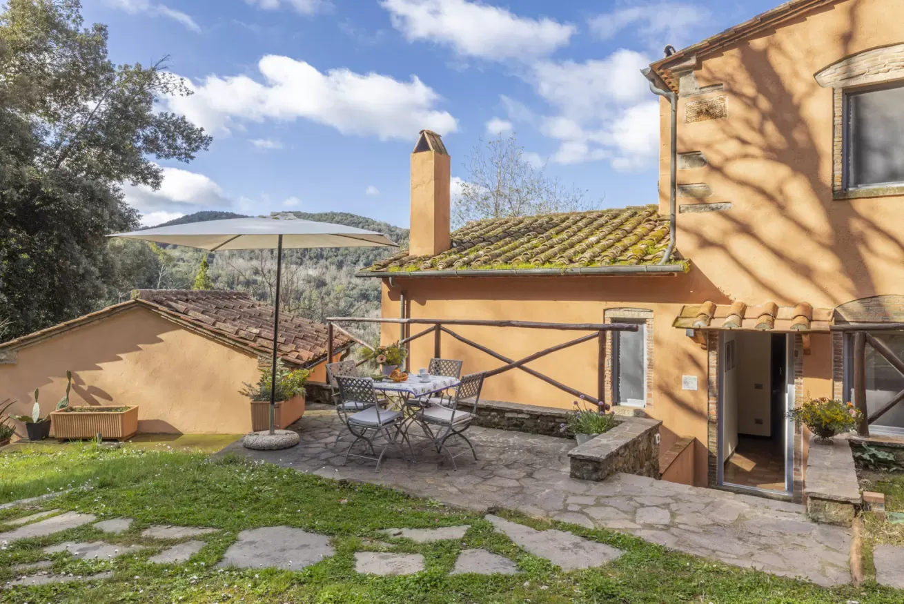 Cortile di una casa in campagna con tavolo all’aperto, ombrellone e vista sulle colline