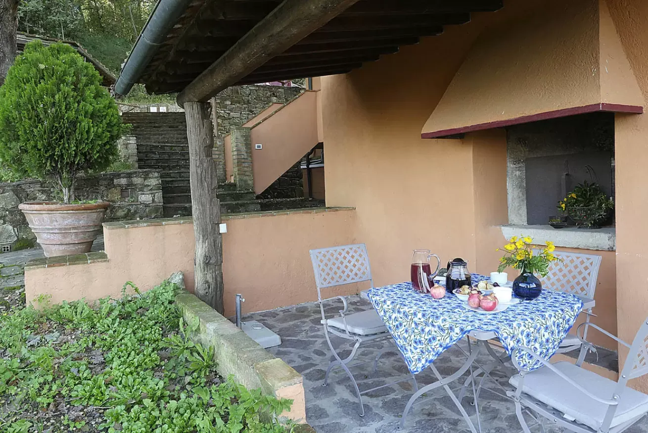 Tavolo apparecchiato su un patio all’aperto accanto a una casa, con piante e scale in pietra