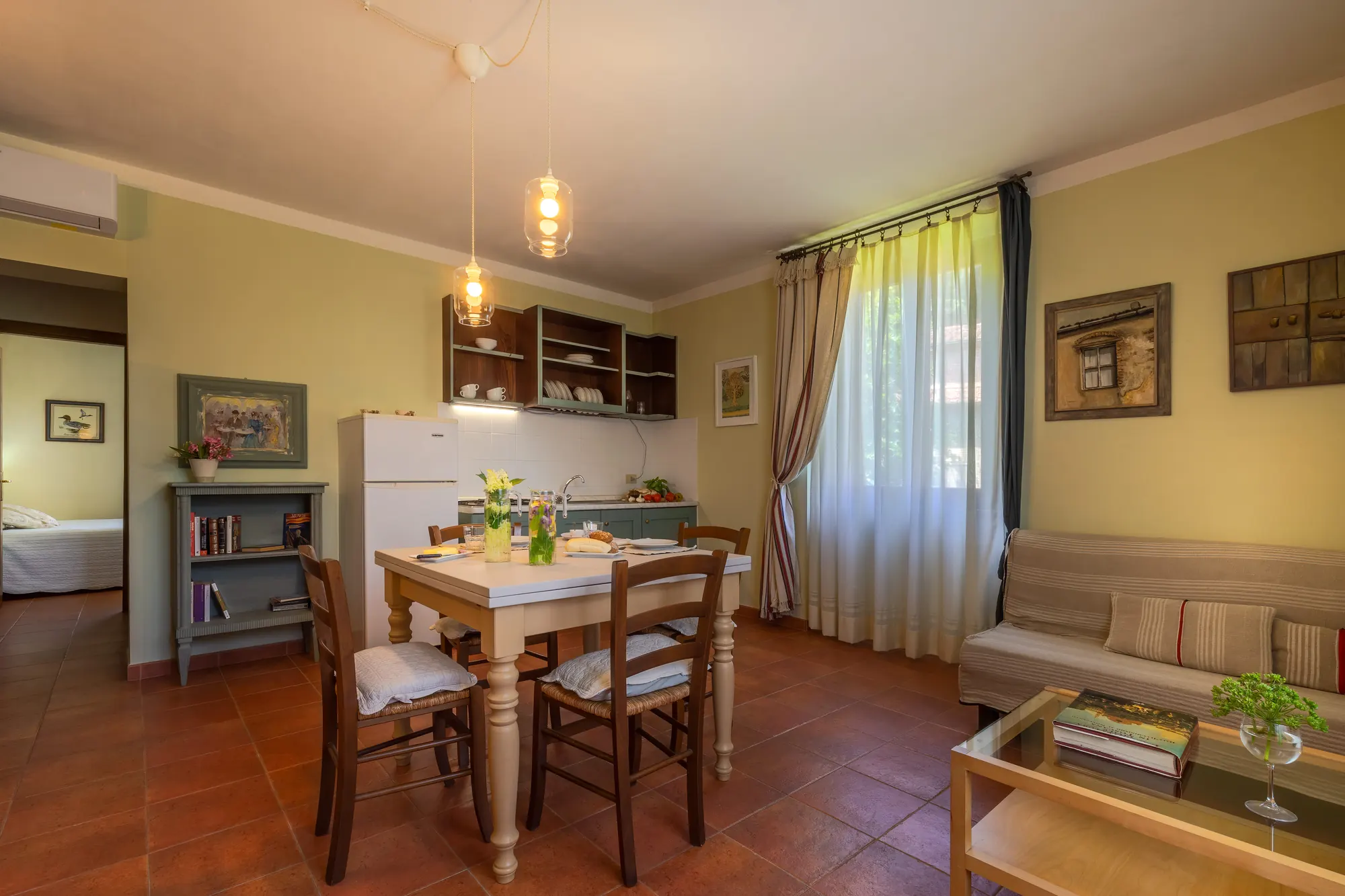 Soggiorno con angolo cucina e tavolo da pranzo apparecchiato, illuminato da luce naturale