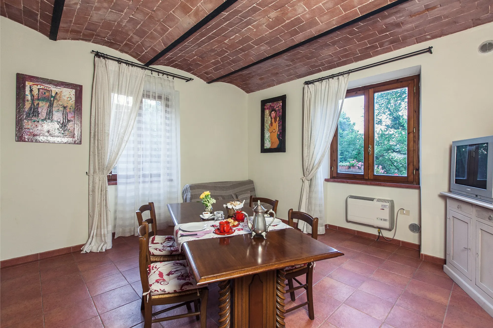 Sala da pranzo con tavolo apparecchiato, sedie, finestre e soffitto a volta in mattoni
