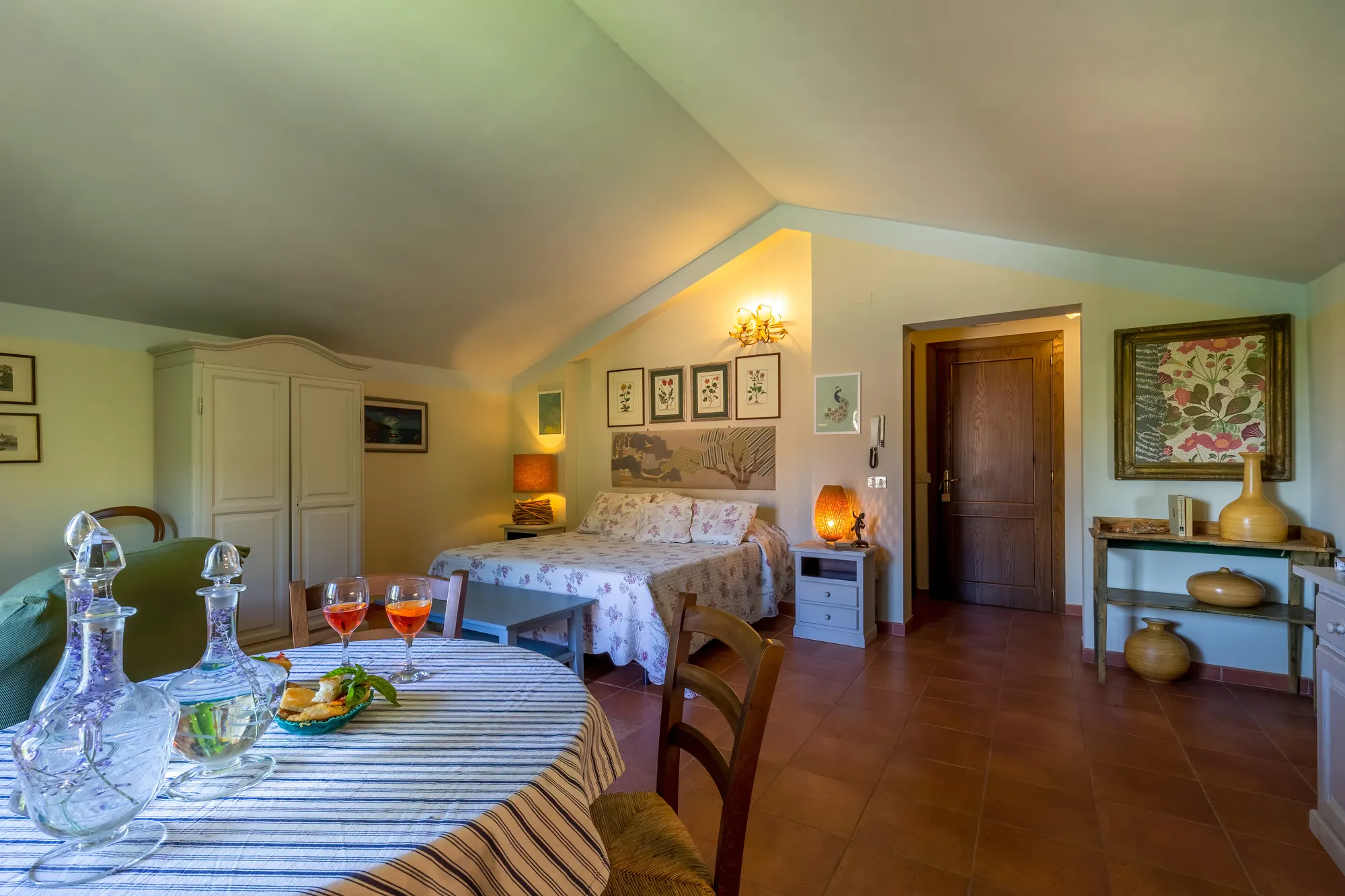 Camera da letto con tavolo apparecchiato in primo piano, letto matrimoniale e arredi rustici in una stanza mansardata