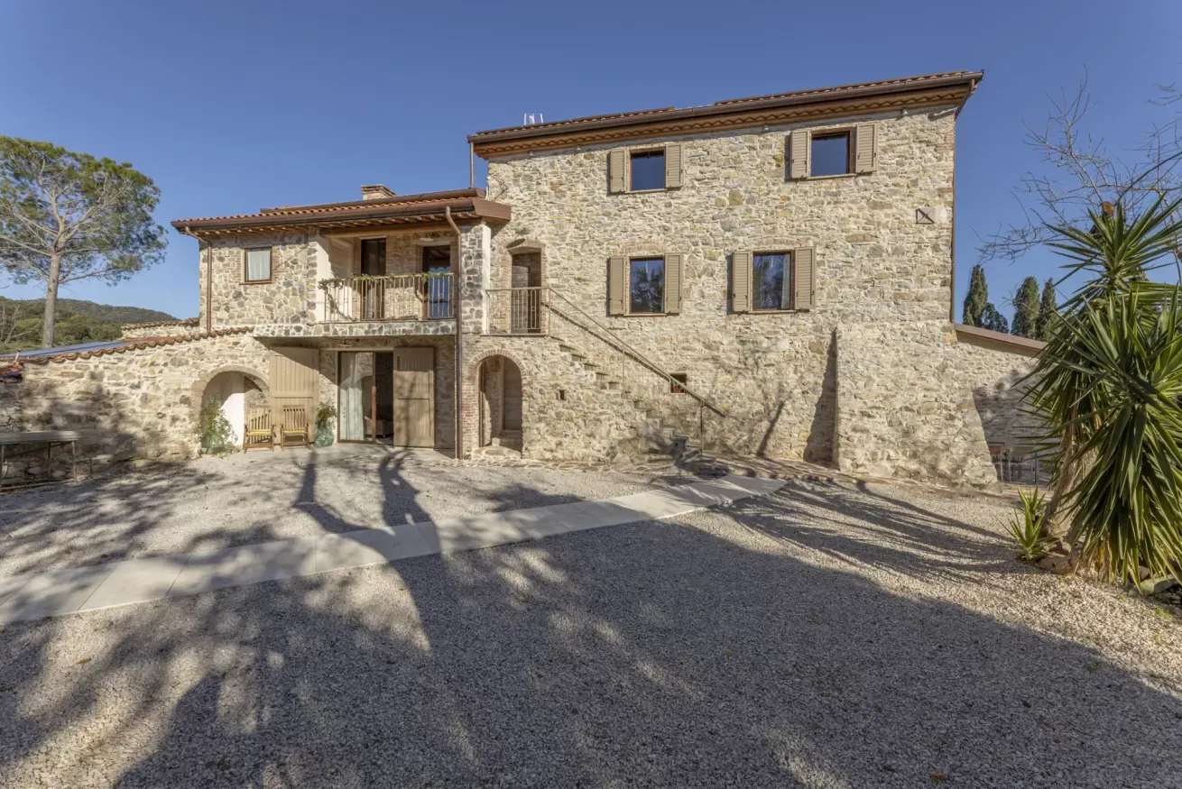 Casa in pietra a più piani con cortile ghiaioso e cielo sereno