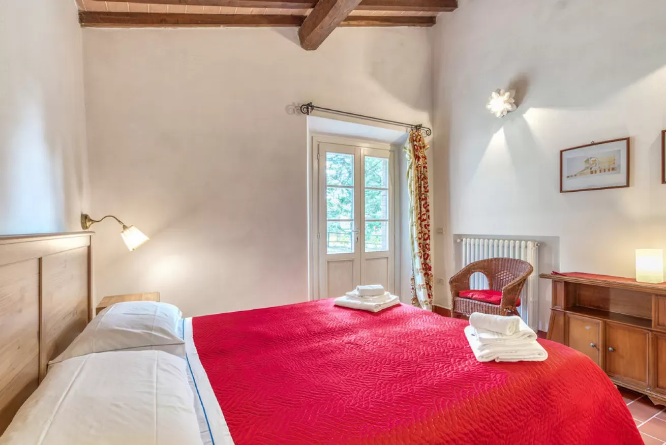 Bedroom with a red bedspread, wicker chair, and French doors to the outside