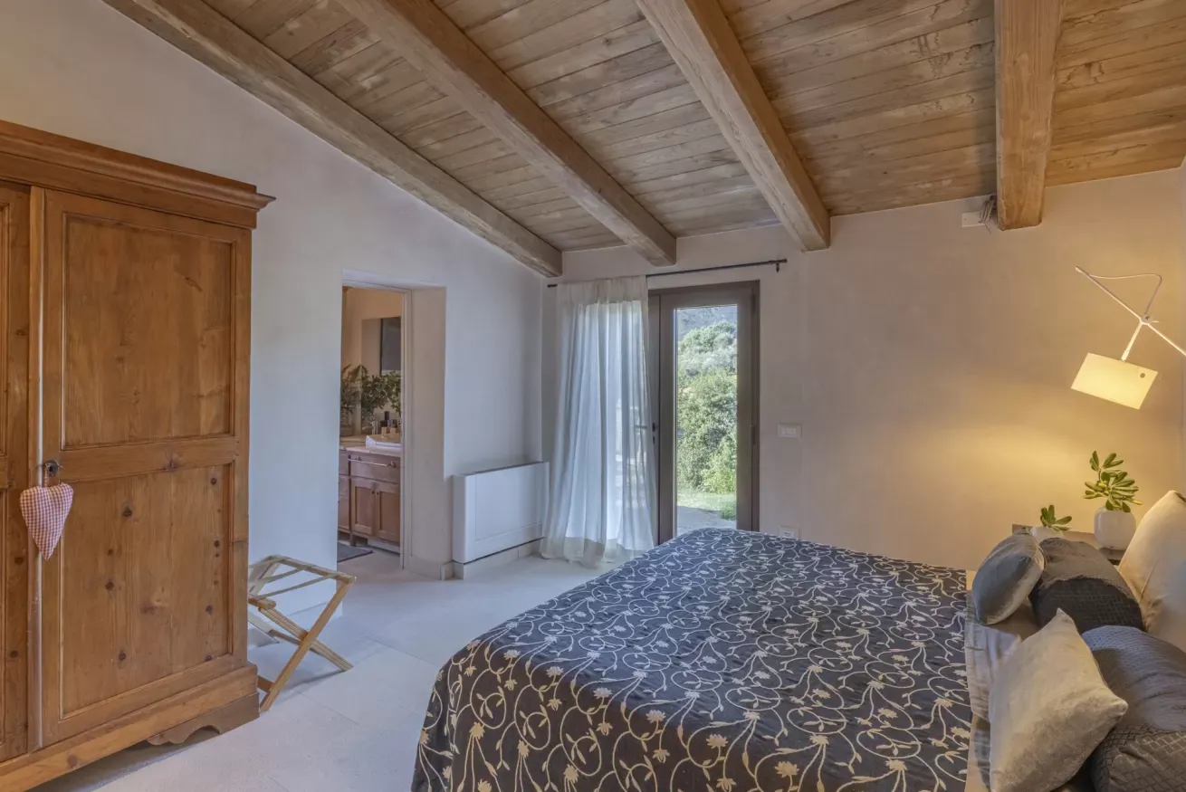 Camera da letto luminosa con soffitto in legno, letto matrimoniale e porta finestra sul verde